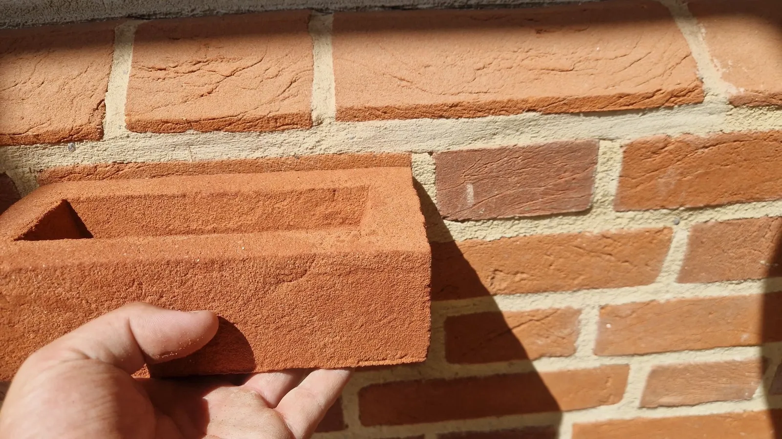 Close view of a handmade-style red brick being checked against a finished wall