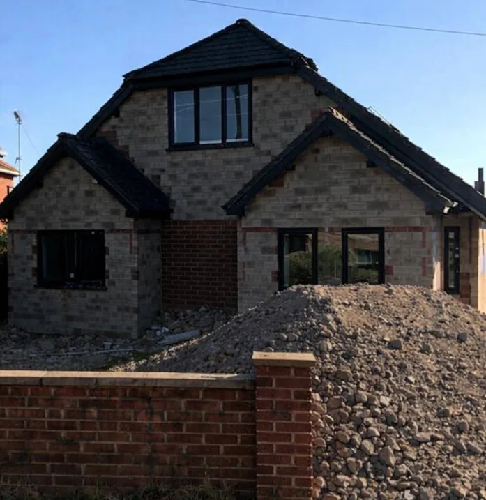 Detached new build in grey and red brick with the roof on and groundworks still open